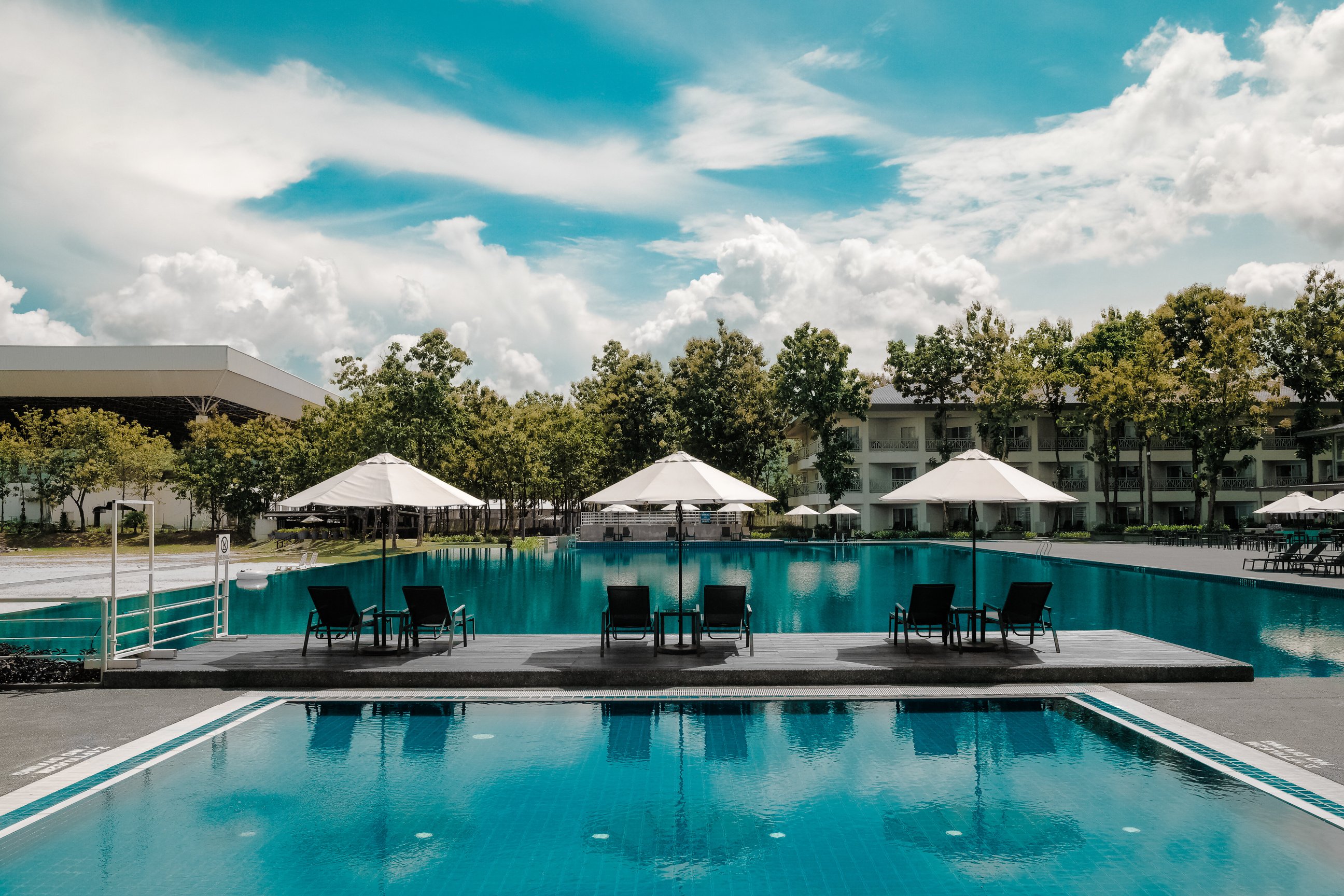 Black Outdoor Lounge Chair in Between Blue Swimming Pool Under White Cloudy Blue Sky